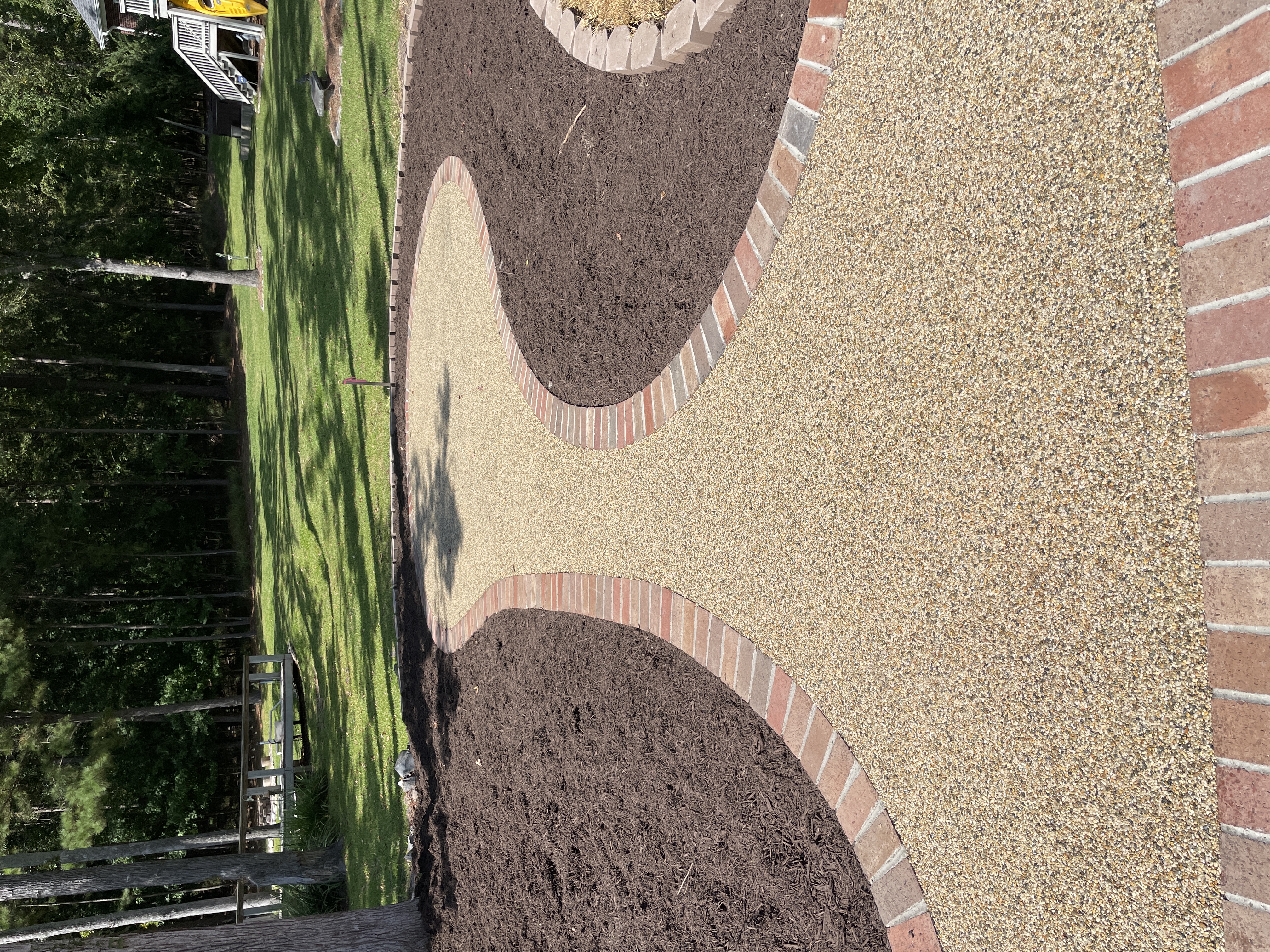 Winding resin rock pathway with brick border in residential backyard
