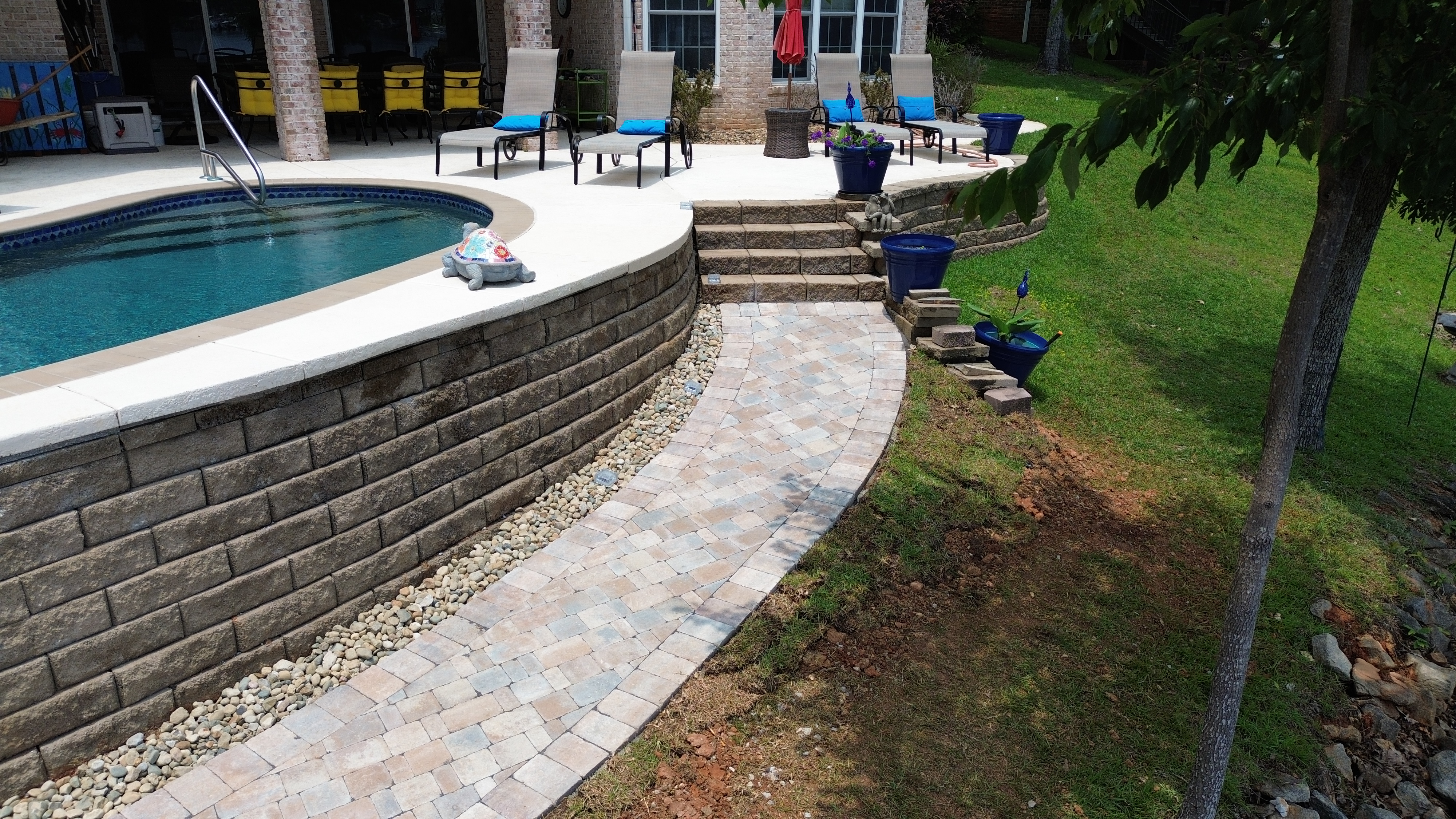 Curved paver walkway alongside pool retaining wall with stone steps
